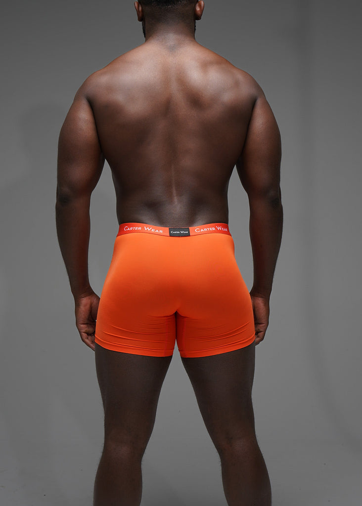 Person wearing bright orange boxer briefs with a gray background